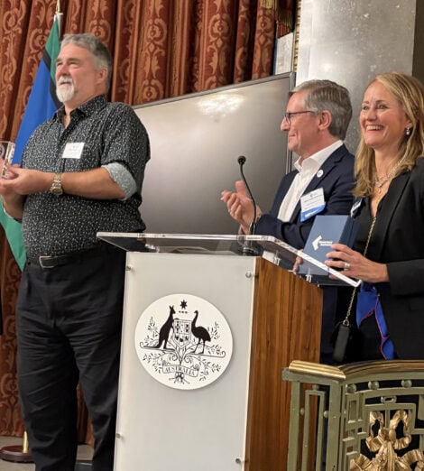 A smiling Terry Hartmann holding the Biometrics Institute’s Lifetime Achievement Award alongside Biometrics Institute Chairman, Jakob Glynstrup and Institute CEO, Isabelle Moeller.